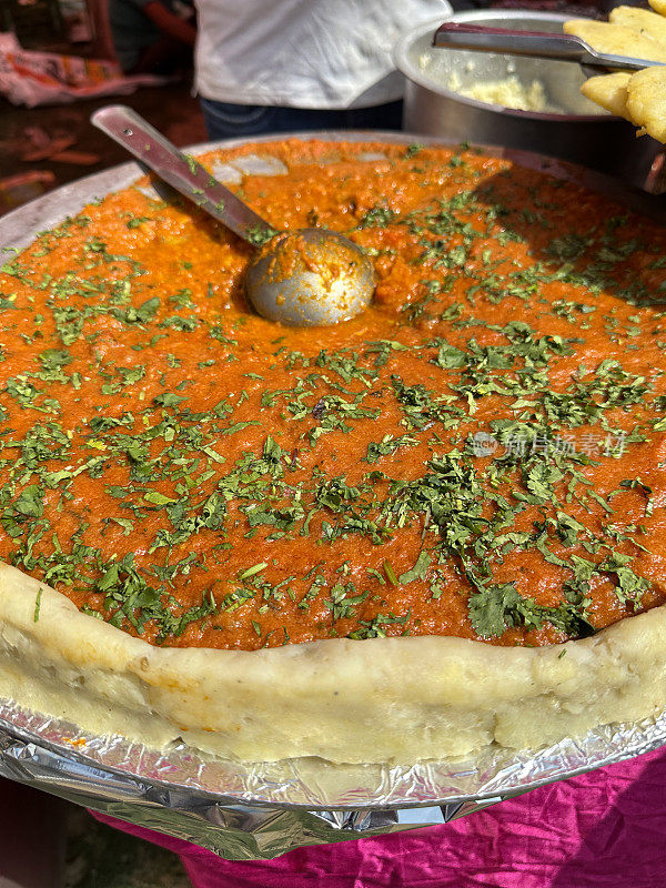 特写图像的印度街头小吃摊餐饮菜Pav bhaji(厚蔬菜咖喱)，香菜装饰，金属服务勺，面目全非的街头小吃摊提供流行的快餐菜，重点在前景